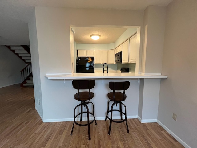 kitchen featuring white cabinetry, sink, a kitchen breakfast bar, kitchen peninsula, and black appliances