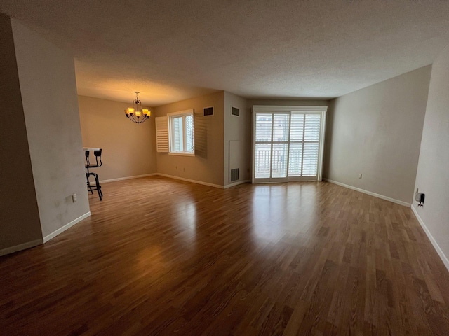 unfurnished living room with hardwood / wood-style flooring, a textured ceiling, and an inviting chandelier