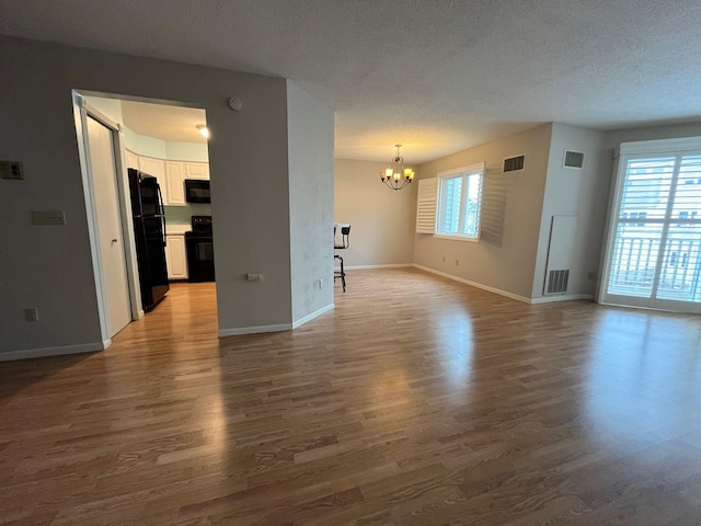 unfurnished living room featuring hardwood / wood-style floors, a textured ceiling, and a notable chandelier