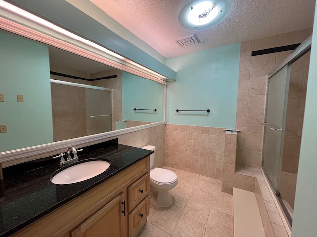 bathroom featuring vanity, a textured ceiling, tile walls, toilet, and a shower with shower door