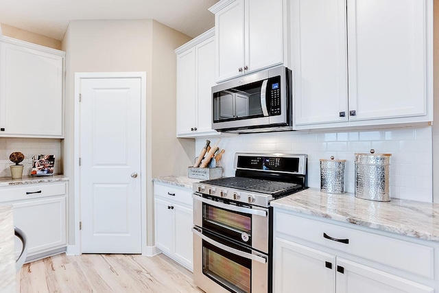 kitchen featuring backsplash, light wood-type flooring, appliances with stainless steel finishes, light stone counters, and white cabinetry