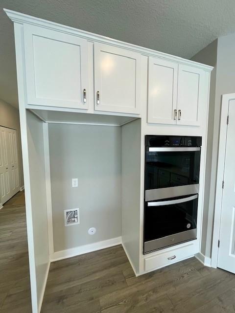 interior space with double oven, a textured ceiling, white cabinets, and dark wood-style flooring