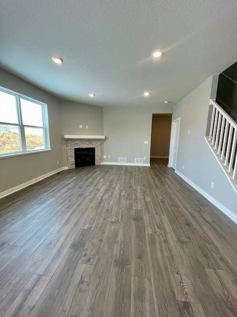 unfurnished living room with a textured ceiling, a fireplace, baseboards, and dark wood-type flooring