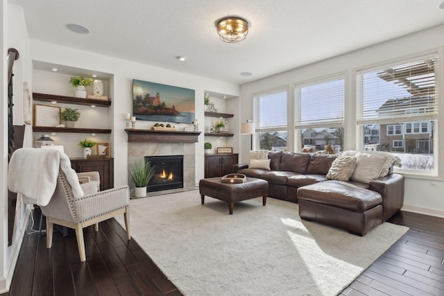 living area with a textured ceiling, a fireplace, baseboards, built in features, and hardwood / wood-style floors