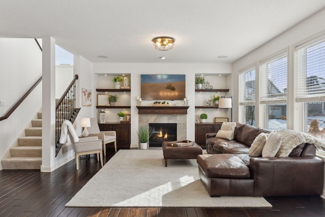 living room with built in shelves, a fireplace, stairway, dark wood-type flooring, and a textured ceiling