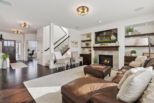 living room featuring dark wood-style flooring, stairway, a fireplace, and built in features