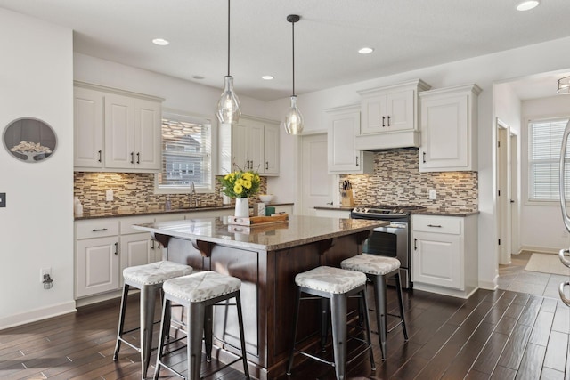 kitchen featuring a center island, dark wood finished floors, stainless steel range with electric cooktop, white cabinetry, and a kitchen breakfast bar