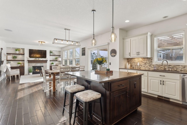 kitchen featuring decorative backsplash, dark wood-type flooring, a kitchen island, dark stone countertops, and a lit fireplace