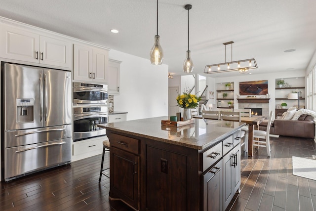 kitchen featuring a breakfast bar, a warm lit fireplace, stainless steel appliances, and dark wood-type flooring