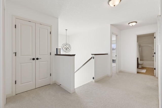 corridor featuring baseboards, light colored carpet, a textured ceiling, and an upstairs landing