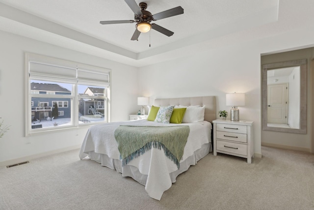 bedroom with a tray ceiling, light colored carpet, visible vents, and baseboards