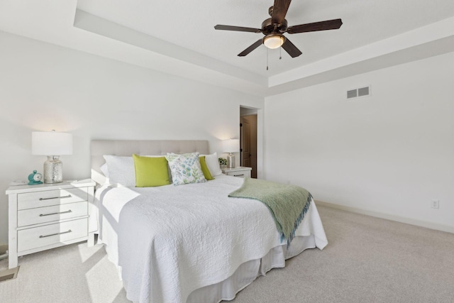 bedroom with light carpet, baseboards, visible vents, a raised ceiling, and ceiling fan