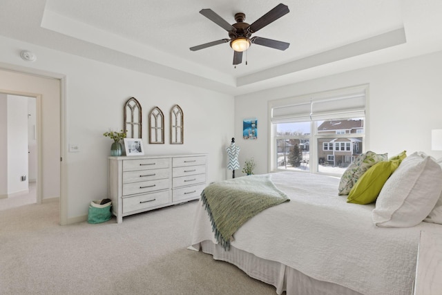 bedroom with light carpet, ceiling fan, baseboards, and a raised ceiling