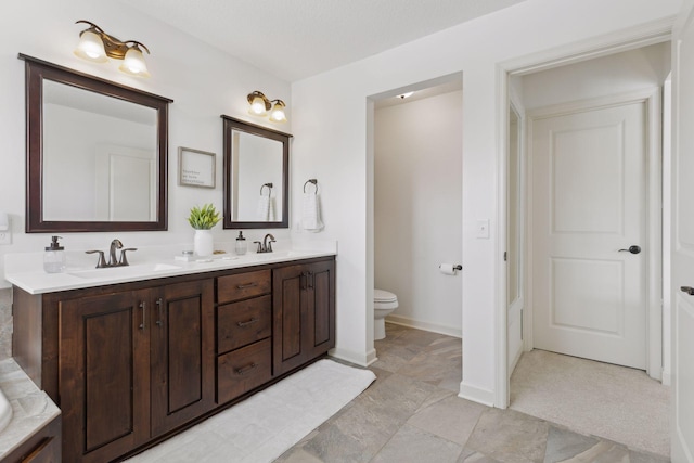 bathroom with toilet, double vanity, baseboards, and a sink