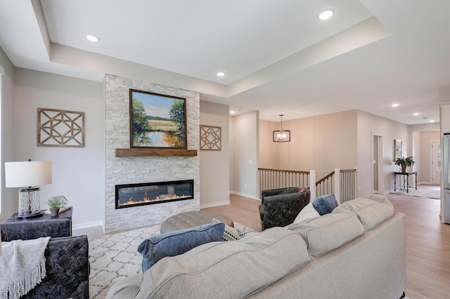 living room featuring a raised ceiling, a stone fireplace, and light hardwood / wood-style flooring