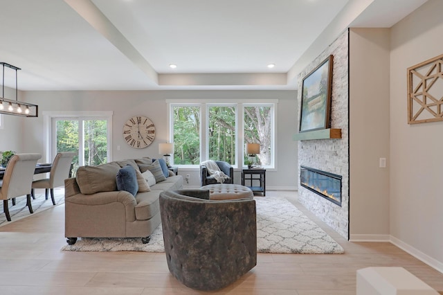 living room featuring a stone fireplace, a healthy amount of sunlight, and light wood-type flooring