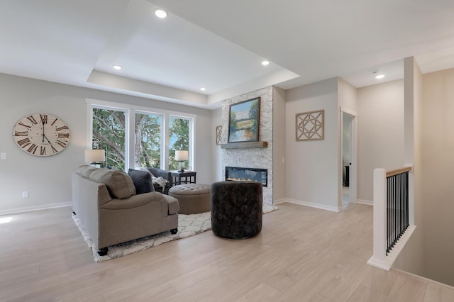 living room with light hardwood / wood-style floors, a stone fireplace, and a tray ceiling