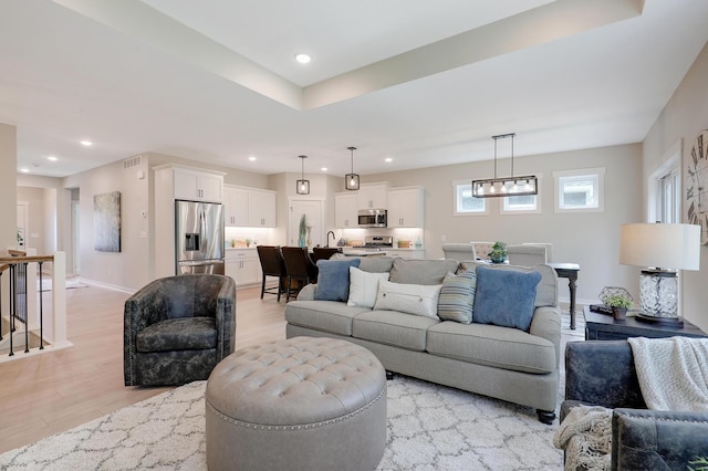 living room featuring a tray ceiling, an inviting chandelier, and light wood-type flooring