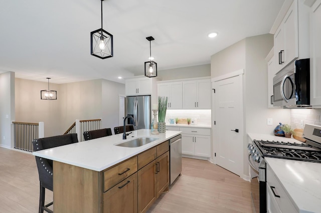 kitchen with sink, stainless steel appliances, white cabinetry, and an island with sink