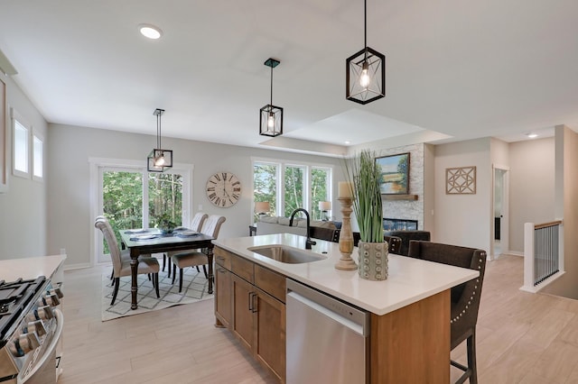 kitchen with sink, hanging light fixtures, stainless steel appliances, a stone fireplace, and a center island with sink