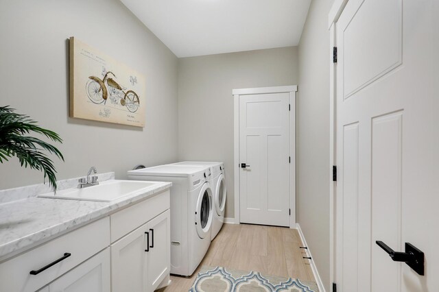 laundry room with washing machine and dryer, cabinets, sink, and light hardwood / wood-style floors