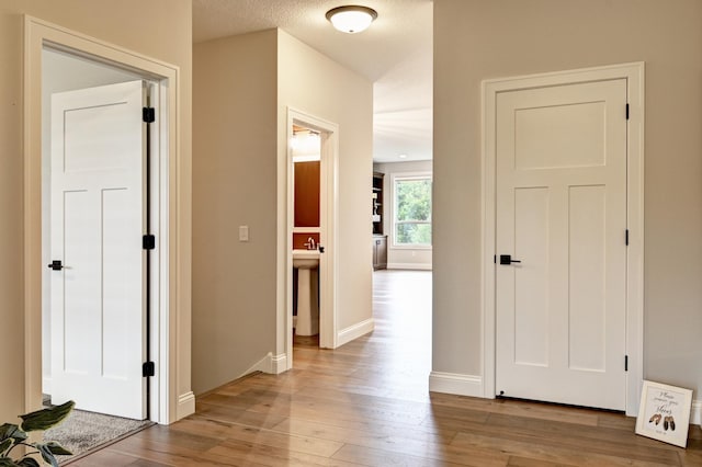 corridor with a textured ceiling and light hardwood / wood-style flooring