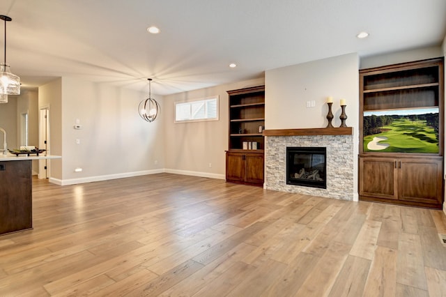 unfurnished living room featuring built in shelves, light wood-type flooring, a fireplace, and an inviting chandelier