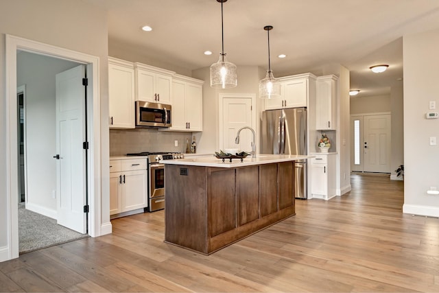 kitchen featuring light wood-type flooring, stainless steel appliances, pendant lighting, a center island with sink, and white cabinets