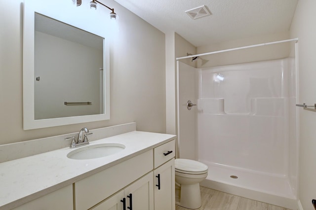 bathroom with a textured ceiling, vanity, a shower, hardwood / wood-style floors, and toilet