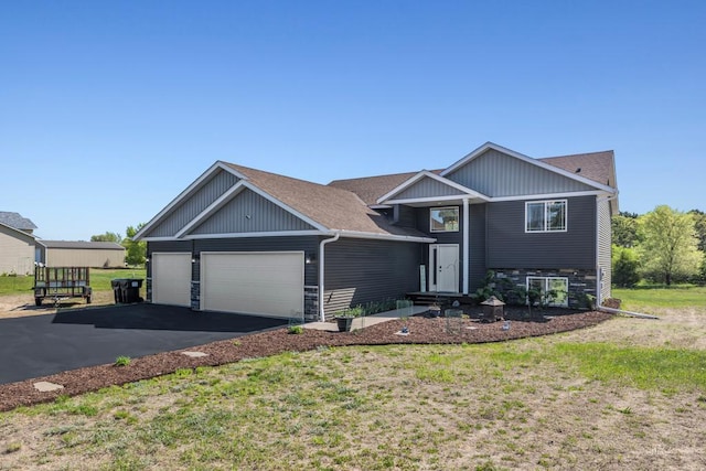 view of front facade featuring an attached garage, driveway, a front yard, and stone siding