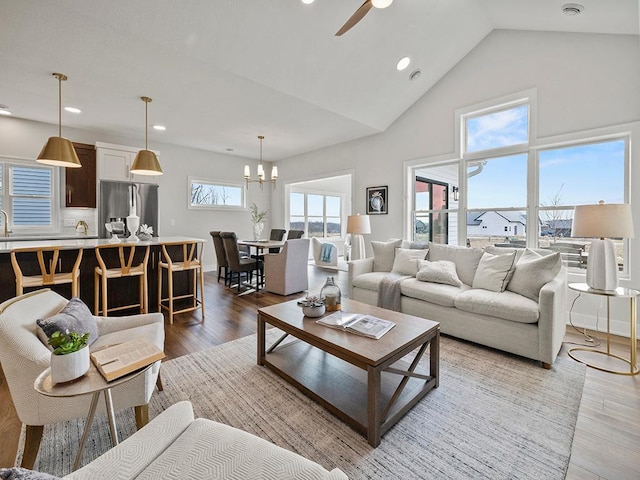 living room with hardwood / wood-style floors, high vaulted ceiling, ceiling fan with notable chandelier, and sink