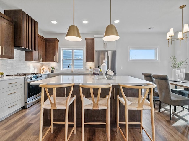 kitchen with backsplash, stainless steel appliances, decorative light fixtures, and wood-type flooring