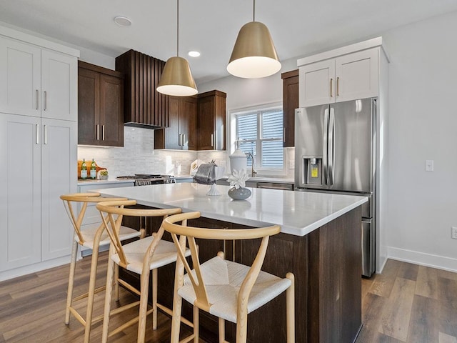 kitchen featuring a kitchen bar, stainless steel refrigerator with ice dispenser, dark wood-type flooring, decorative light fixtures, and a kitchen island