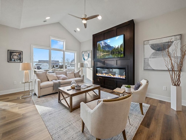 living room featuring ceiling fan, a large fireplace, light hardwood / wood-style floors, and high vaulted ceiling