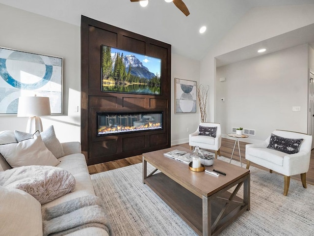 living room with ceiling fan, a large fireplace, light hardwood / wood-style floors, and vaulted ceiling