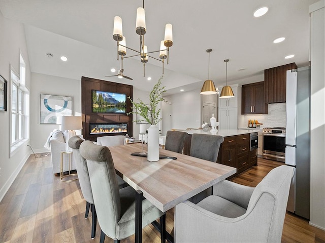 dining area featuring a large fireplace, a healthy amount of sunlight, a notable chandelier, and wood-type flooring