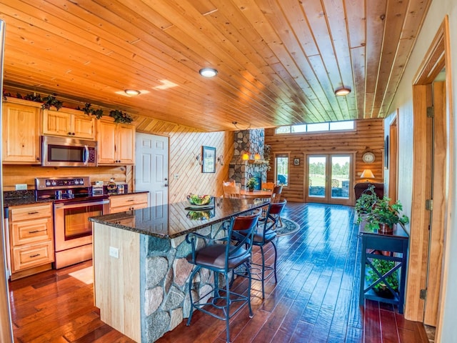 kitchen with appliances with stainless steel finishes, dark hardwood / wood-style flooring, rustic walls, wood ceiling, and a breakfast bar