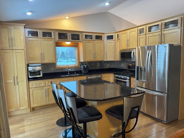 kitchen featuring sink, stainless steel appliances, vaulted ceiling, decorative backsplash, and a kitchen island