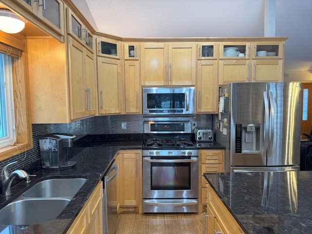 kitchen with sink, dark stone countertops, light wood-type flooring, tasteful backsplash, and stainless steel appliances