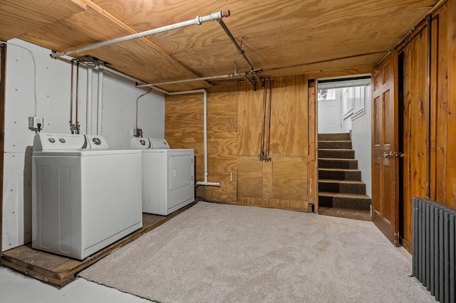 laundry area with radiator heating unit, washer and clothes dryer, and wooden walls