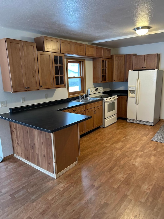 kitchen with a textured ceiling, kitchen peninsula, white appliances, and hardwood / wood-style flooring