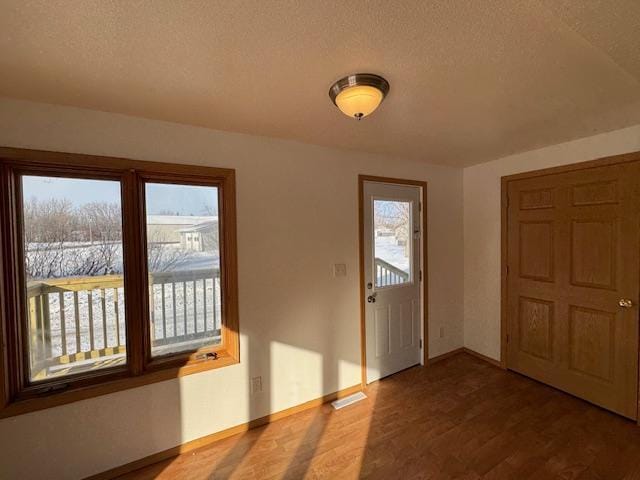 foyer featuring a textured ceiling, wood finished floors, visible vents, and baseboards