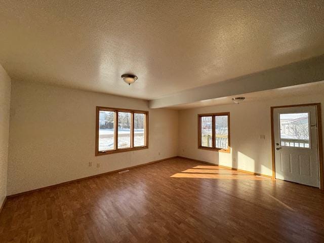 spare room featuring a textured ceiling, baseboards, wood finished floors, and a healthy amount of sunlight