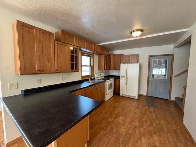 kitchen with a peninsula, white appliances, wood finished floors, brown cabinets, and dark countertops