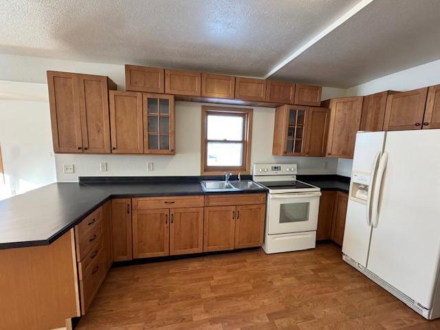 kitchen with white appliances, brown cabinetry, dark countertops, and glass insert cabinets