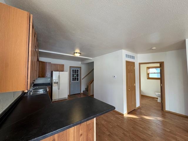 kitchen with dark wood-style floors, dark countertops, visible vents, brown cabinetry, and white fridge with ice dispenser