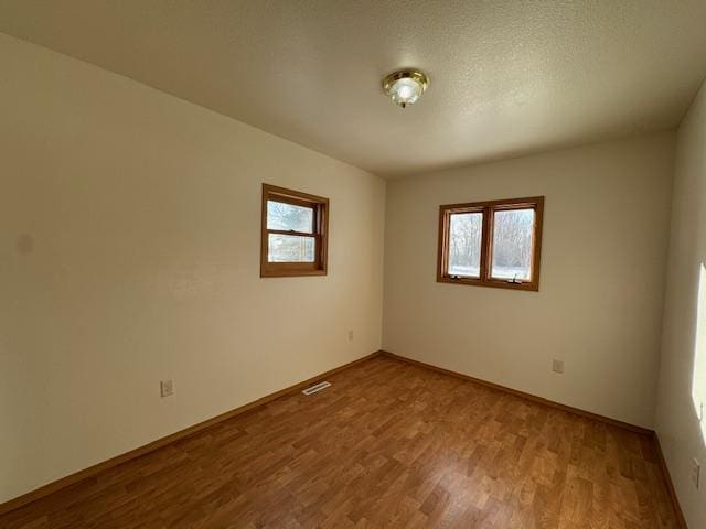 empty room with baseboards, visible vents, a textured ceiling, and light wood finished floors