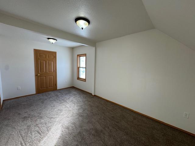 spare room featuring lofted ceiling and dark carpet