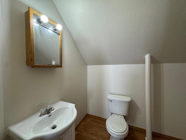 half bath with a textured ceiling, toilet, wood finished floors, a sink, and vaulted ceiling