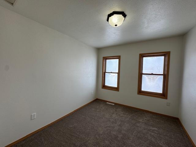 spare room with dark colored carpet, visible vents, a textured ceiling, and baseboards